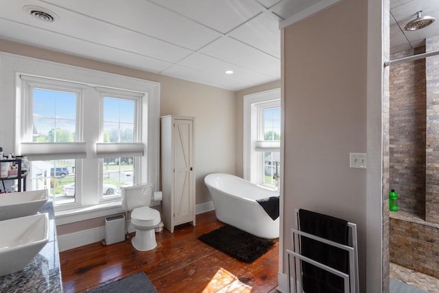 bathroom with wood-type flooring, visible vents, baseboards, a freestanding bath, and a tile shower
