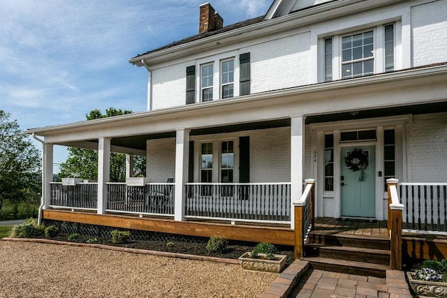 doorway to property with covered porch, brick siding, and a chimney