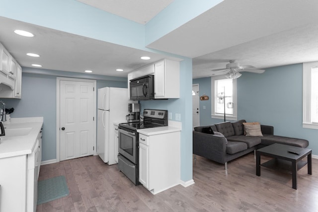 kitchen featuring black microwave, light wood-type flooring, a sink, white cabinets, and stainless steel electric stove