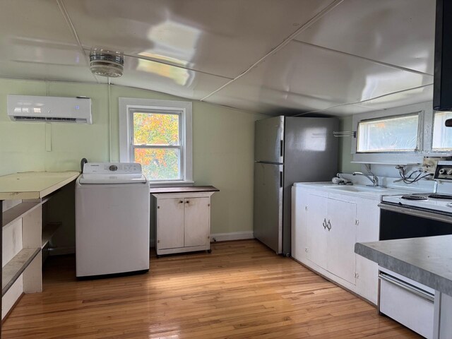 kitchen featuring electric stove, a wall mounted air conditioner, light hardwood / wood-style floors, a healthy amount of sunlight, and washer / clothes dryer