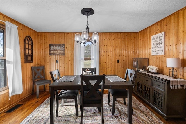 dining room featuring a notable chandelier, hardwood / wood-style flooring, a textured ceiling, and wood walls