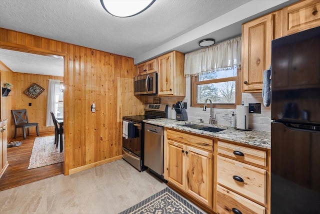 kitchen with wooden walls, sink, stainless steel appliances, light stone countertops, and a textured ceiling