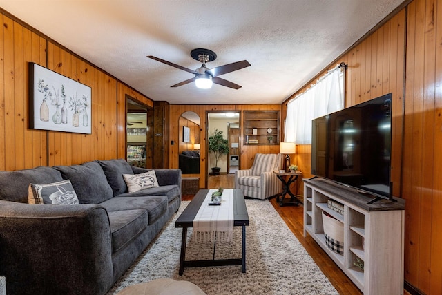 living room with ceiling fan, wood-type flooring, a textured ceiling, and wood walls