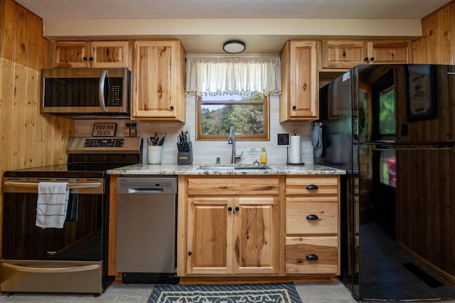 kitchen featuring wooden walls, sink, decorative backsplash, light stone counters, and stainless steel appliances