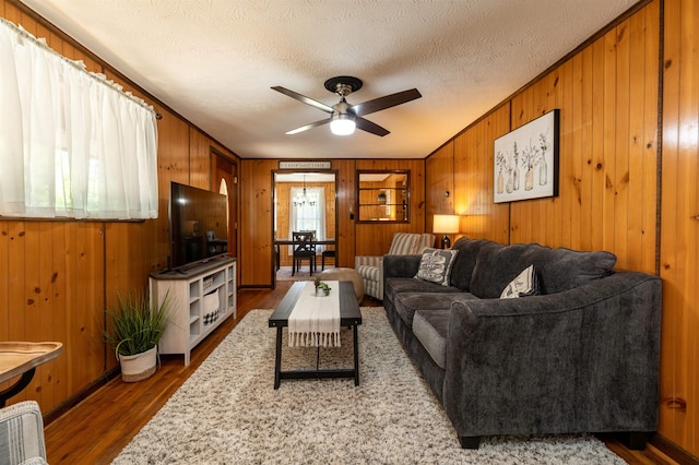 living room with ceiling fan, wooden walls, hardwood / wood-style floors, and a textured ceiling