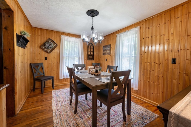 dining room featuring wooden walls, dark hardwood / wood-style floors, a chandelier, and a textured ceiling