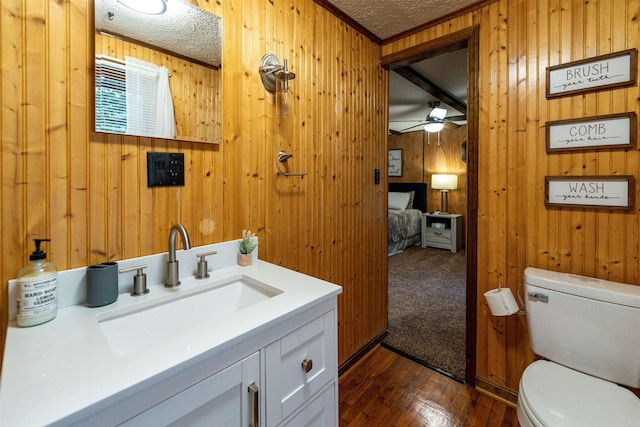 bathroom with wood walls, hardwood / wood-style flooring, vanity, toilet, and a textured ceiling