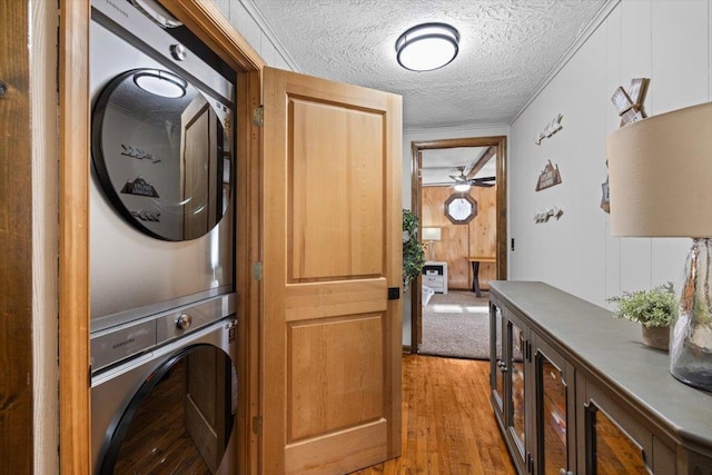 laundry room with wooden walls, stacked washing maching and dryer, a textured ceiling, and light hardwood / wood-style flooring