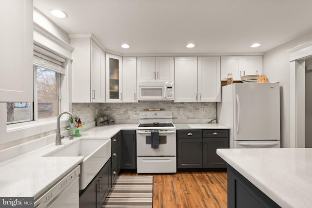 kitchen with white cabinetry, sink, light wood-type flooring, backsplash, and white appliances