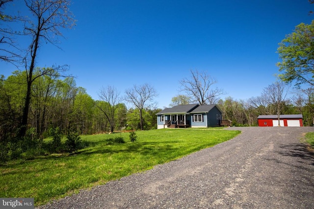 ranch-style house with a detached garage, dirt driveway, an outbuilding, and a front lawn