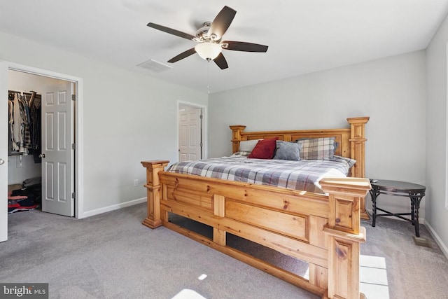 bedroom featuring ceiling fan, light colored carpet, a walk in closet, baseboards, and visible vents