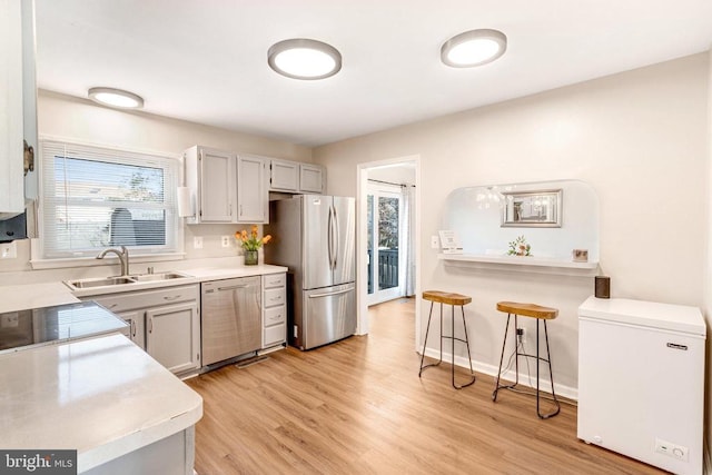 kitchen with light wood finished floors, baseboards, a breakfast bar, stainless steel appliances, and a sink