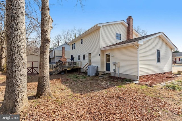 back of house with a shed, entry steps, a wooden deck, a chimney, and an outdoor structure