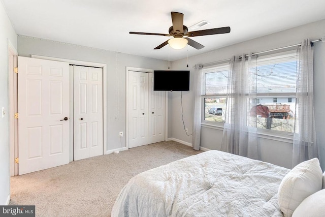 carpeted bedroom with baseboards, two closets, and ceiling fan