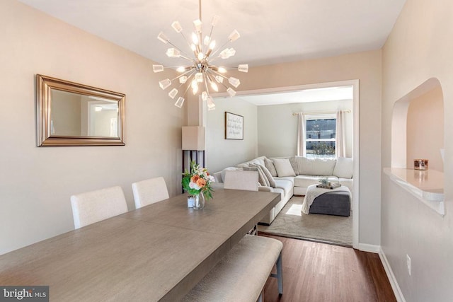 dining area featuring a chandelier, arched walkways, baseboards, and wood finished floors