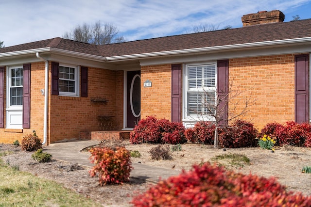 doorway to property with a shingled roof, a chimney, and brick siding