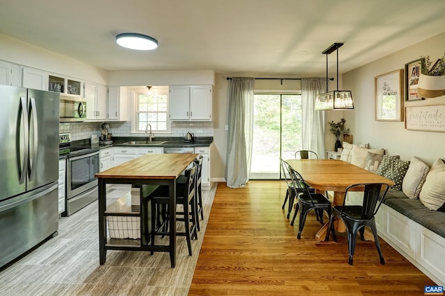 kitchen featuring light wood-type flooring, white cabinetry, a sink, appliances with stainless steel finishes, and backsplash