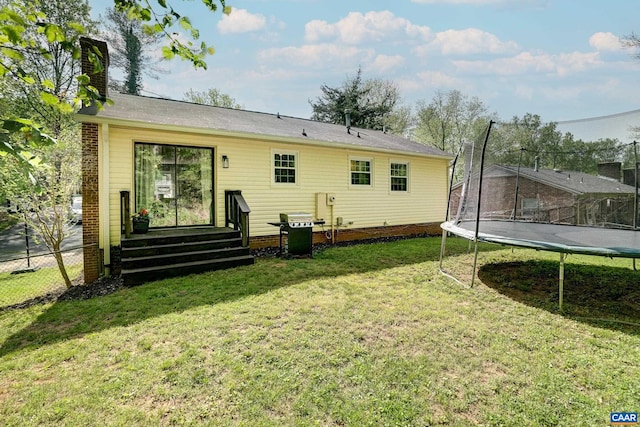 rear view of house with a lawn, fence, a trampoline, and a chimney