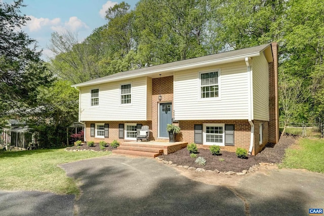 bi-level home with brick siding, fence, covered porch, and a front yard