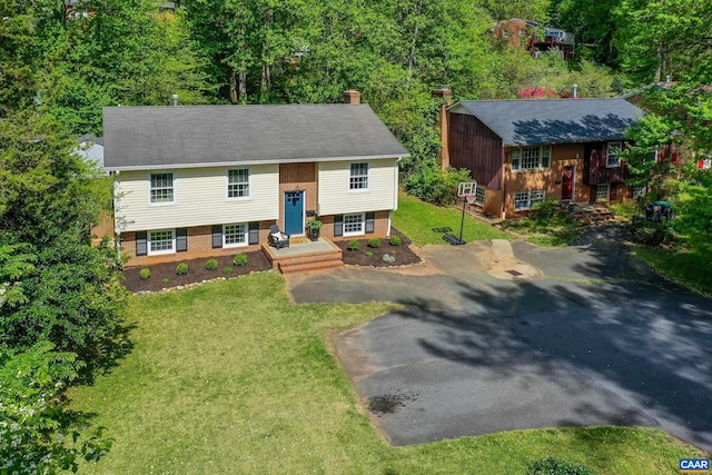 bi-level home with brick siding, a chimney, a front lawn, and aphalt driveway