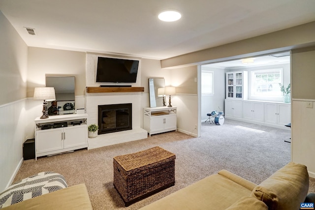 carpeted living room with visible vents, wainscoting, and a fireplace