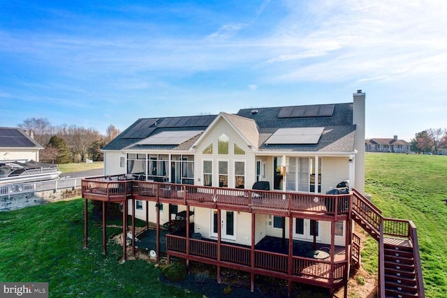 back of house featuring a chimney, stairs, a deck, a yard, and roof mounted solar panels