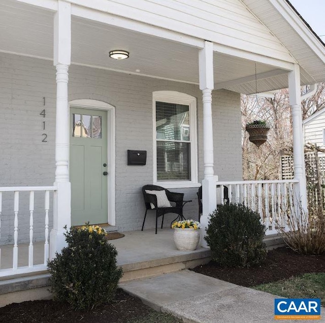 doorway to property with a porch and brick siding