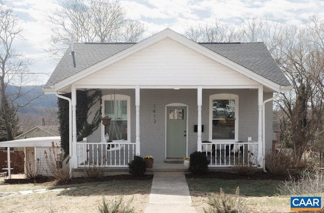 bungalow with a shingled roof, covered porch, and brick siding