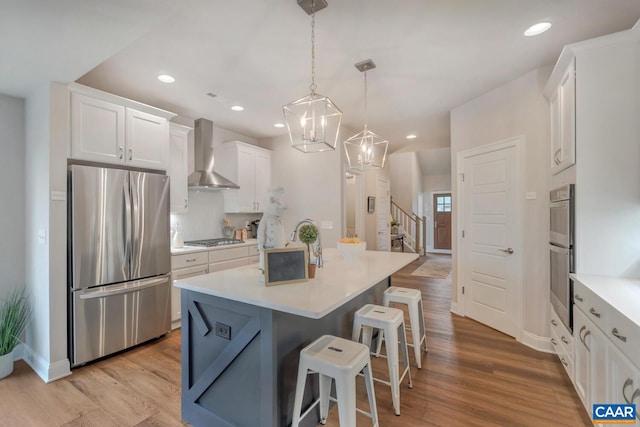 kitchen featuring pendant lighting, a breakfast bar, appliances with stainless steel finishes, white cabinetry, and wall chimney exhaust hood