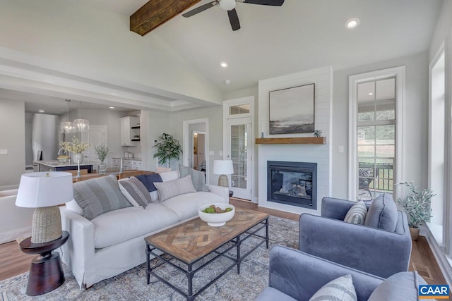 living room featuring ceiling fan with notable chandelier, vaulted ceiling with beams, hardwood / wood-style floors, and a large fireplace