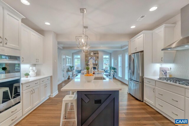 kitchen with appliances with stainless steel finishes, white cabinetry, light wood-style floors, and wall chimney exhaust hood