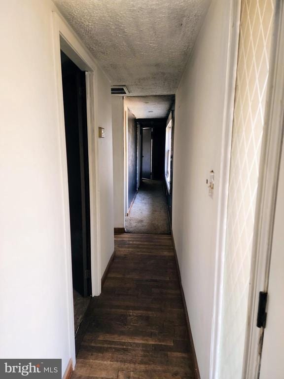 hallway with dark wood-style flooring, a textured ceiling, and baseboards