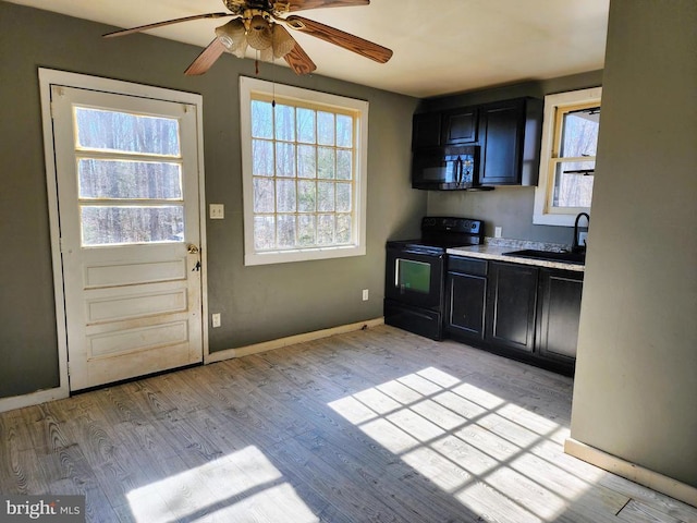 kitchen featuring a sink, baseboards, light wood-type flooring, black appliances, and dark cabinets