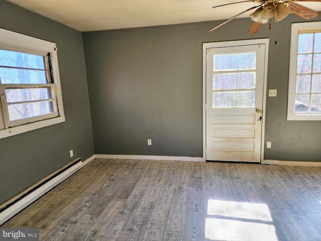 interior space with a baseboard heating unit, plenty of natural light, and wood finished floors