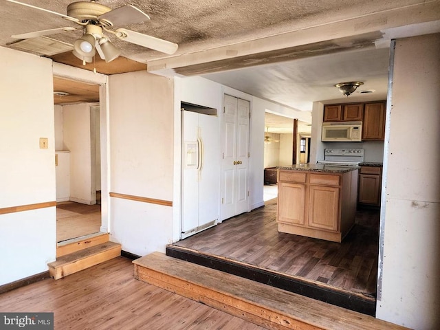 kitchen featuring dark countertops, a center island, white appliances, baseboards, and dark wood-style flooring