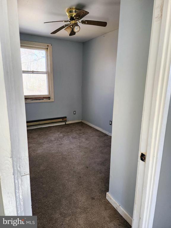 empty room featuring a ceiling fan, a baseboard radiator, baseboards, and dark colored carpet