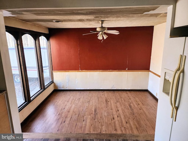 empty room with a ceiling fan, a textured ceiling, baseboards, and wood finished floors