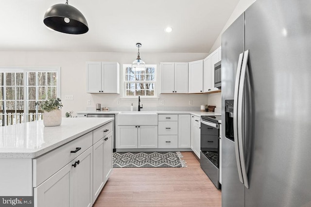 kitchen with appliances with stainless steel finishes, pendant lighting, sink, white cabinets, and light hardwood / wood-style flooring