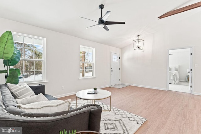 living room featuring ceiling fan with notable chandelier, plenty of natural light, vaulted ceiling, and light wood-type flooring