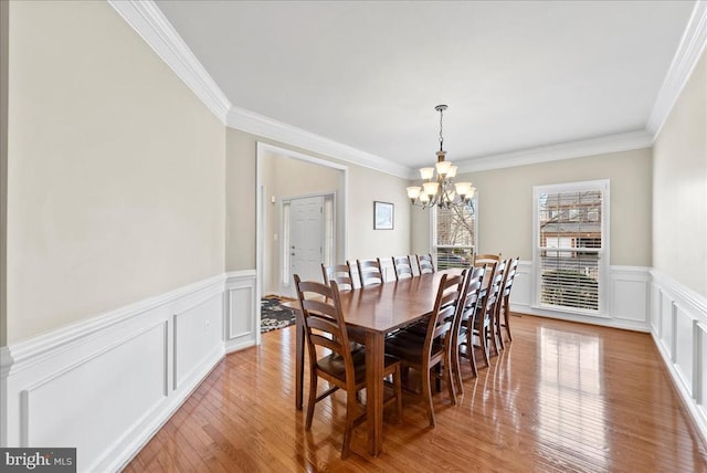 dining area featuring crown molding, wainscoting, an inviting chandelier, and light wood-style floors