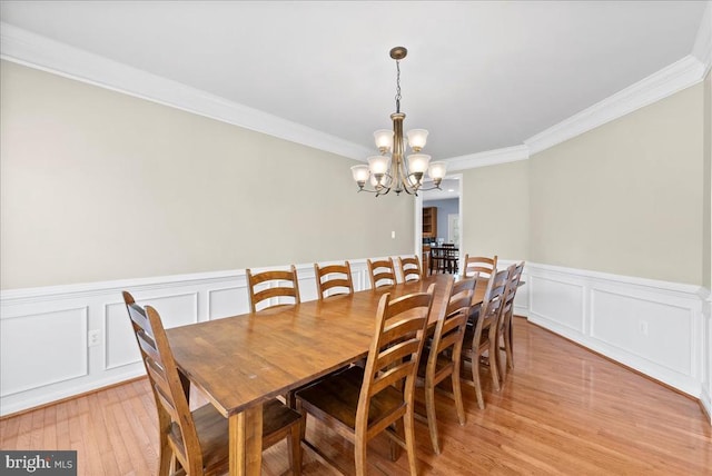 dining room featuring crown molding, wainscoting, light wood-type flooring, and a notable chandelier