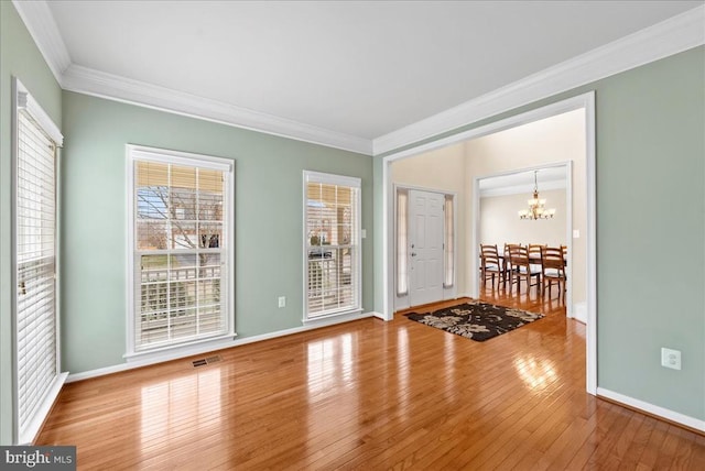 empty room featuring crown molding, visible vents, a notable chandelier, and hardwood / wood-style floors