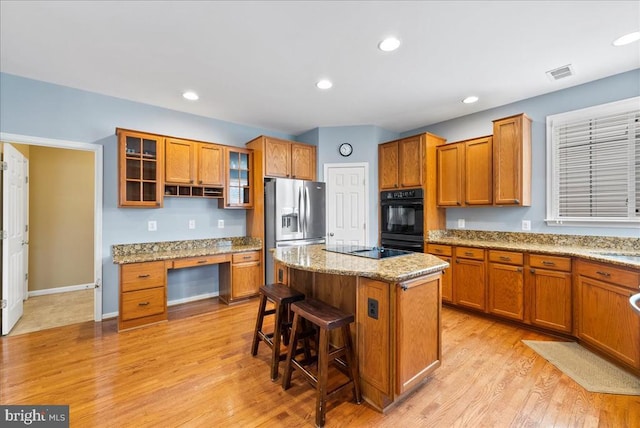 kitchen featuring visible vents, brown cabinetry, a kitchen breakfast bar, a center island, and black appliances