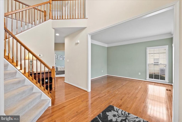 interior space featuring baseboards, stairway, wood finished floors, a high ceiling, and crown molding