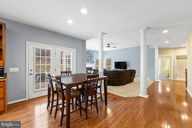 dining space featuring ceiling fan, light wood finished floors, a fireplace, and ornate columns