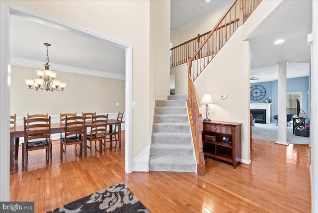 stairs with a fireplace, ornamental molding, wood finished floors, a chandelier, and ornate columns