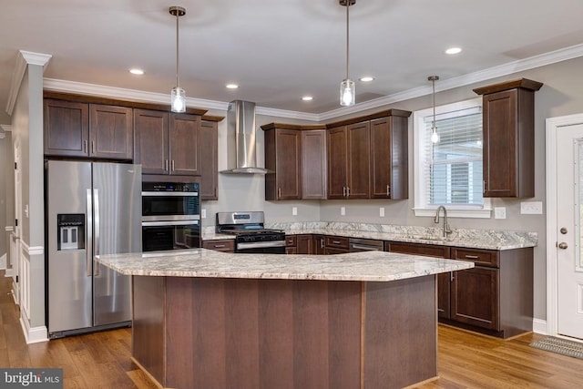 kitchen featuring wall chimney range hood, decorative light fixtures, a kitchen island, and appliances with stainless steel finishes