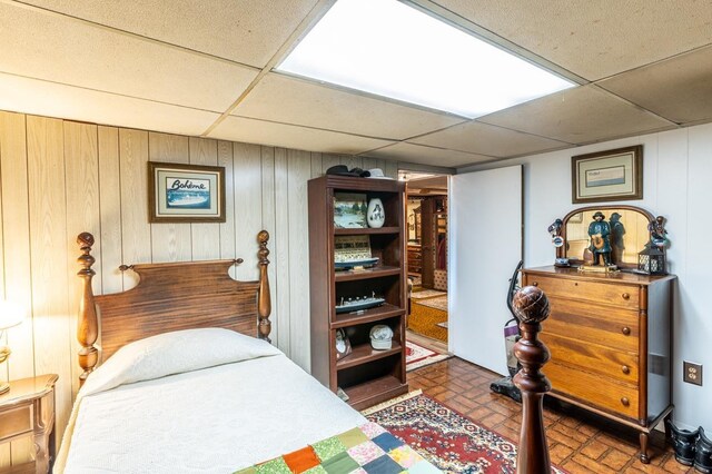 bedroom with a paneled ceiling and wood walls