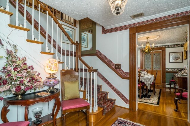 stairway featuring a notable chandelier, crown molding, hardwood / wood-style floors, and a textured ceiling