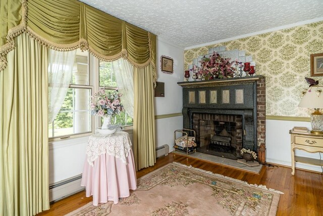 living area with a baseboard heating unit, hardwood / wood-style flooring, a textured ceiling, and a brick fireplace